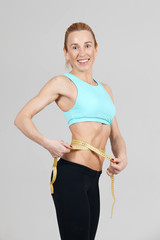 athletic slim woman measuring the size of her waist by the ruler and smiling on the grey background