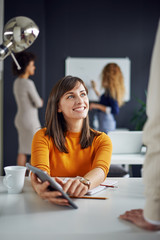 Young woman is talking to his colleague in the office, two women discuss behind her in front of whiteboard