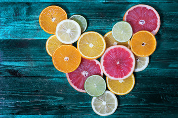 round slices of different citrus folded into the shape of a heart on turquoise wooden background