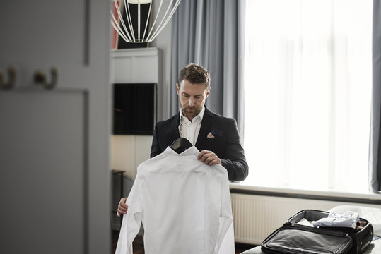 Businessman holding white shirt in coathanger against window at hotel room