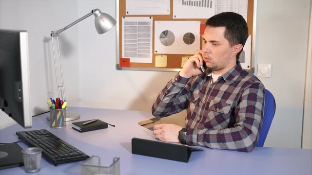 Male manager using smartphone to talk with his client or for other working needs. Classical office scene.