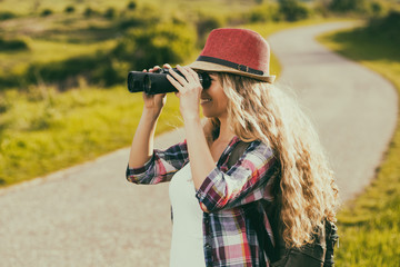 Beautiful young woman at the country road  enjoys looking through binoculars.