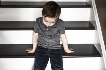 Fototapeta na wymiar one sad little boy sitting on the stairs in house at the day time.