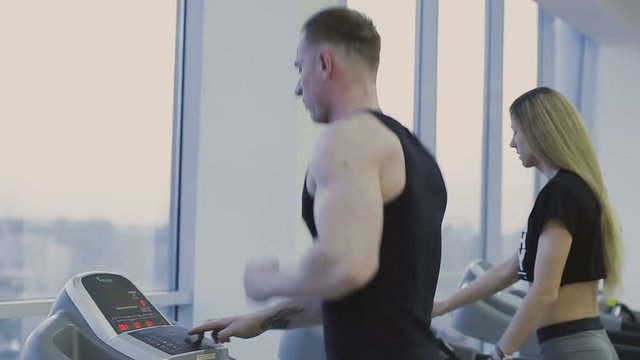 A man and a girl are training on a treadmill in a fitness club