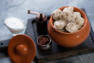 Black wooden serving board with boiled pelmeni in a ceramic pot, studio shot