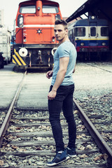 Handsome young man in blue t-shirt in front of train, looking at camera, turning around