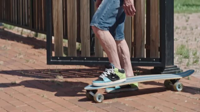 MS Tilt down of young-looking senior man standing at house gate, looking around and starting longboarding in slow motion