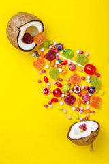 Colorful explosion of candies in coconut on yellow colored background, creative still life, flat lay style, copy space