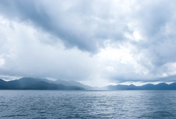 The blue ocean with some rain; mountains and cloudy sky as a background