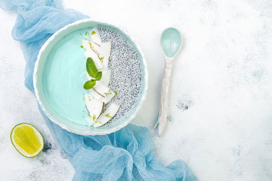 Vegan Blue Spirulina Smoothie And Chia Pudding Bowl Topped With Coconut Flakes And Lime Zest. Overhead, Flat Lay, Top View, Copy Space