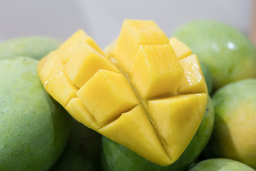 Closeup of mango cubes slices with green mangoes on shelf background