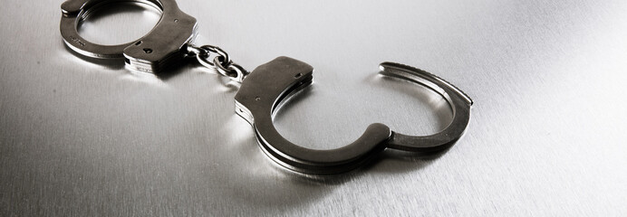 closeup of handcuffs on obscure stainless steel background for prison
