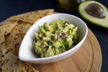 Green homemade Guacamole with chips. black background