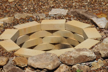 Fire pit made of the yellow aluminous bricks and boulders surrounded by pebbles in the summer garden