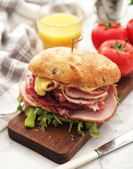 Sandwich with ham and fresh salad and tomatoes served on a wooden board.