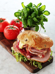 Sandwich with ham and fresh salad and tomatoes served on a wooden board.