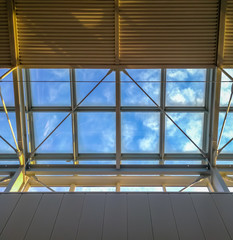 Contemporary transparent plastic roof with modern design, under the roof. Glass panel roof with bright battens under blue sky. Look up through transparent plastic sheet to blue sky.