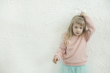 Little princess girl making fun faces on the white brick wall backgtound