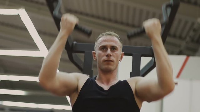 A muscular man in a black T-shirt is training on a fitness machine in a fitness club