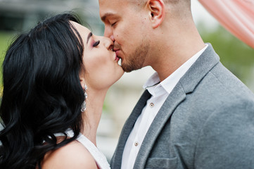 Young fashionable lovely kissed couple against decor arch on wedding anniversary and marriage proposal.