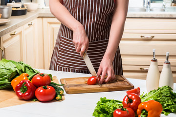 Young woman cooking in the kitchen at home. A woman cuts a tomato and vegetables with a knife.