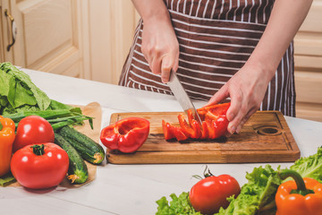 Young woman cooking in the kitchen at home. A woman cuts a pepper and vegetables with a knife.