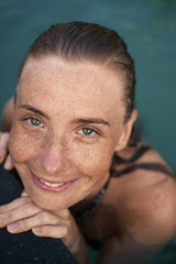 Vertical close-up portrait of beautiful girl with sunspots and wet hair in water