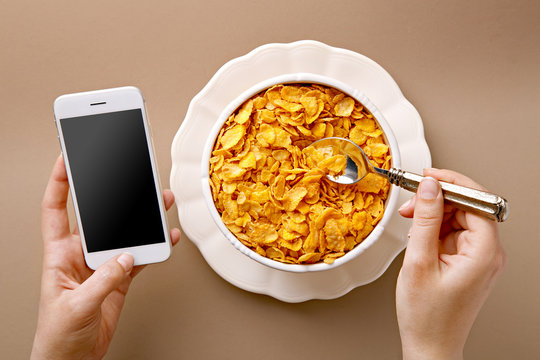 Woman Texting And Eating Healthy Breakfast. View From Above. Hands Holding A Phone And Spoon With Healthy Cereals. Top View