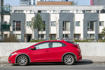 A red car parks in front of a modern apartment