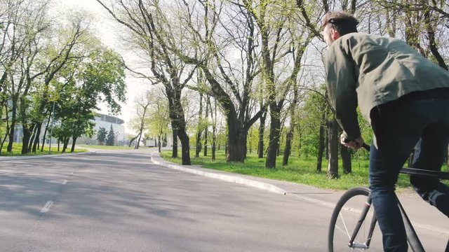 Tracking shot of hipster man riding fixed gear bicycle in park