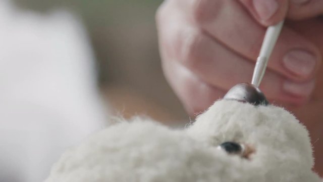 The master draws a nose for a teddy bear in an old-fashioned style. Handmade. Details of teddy bear. A rare collectible toy is a teddy bear. Favorite toy of children is a teddy bear.
