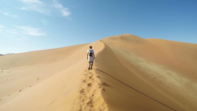 Tourist walking on the scenic dunes of Sossusvlei, Namib desert, Namib Naukluft National Park, Namibia. Afternoon light. Adventure and exploration in Africa. Slow motion.