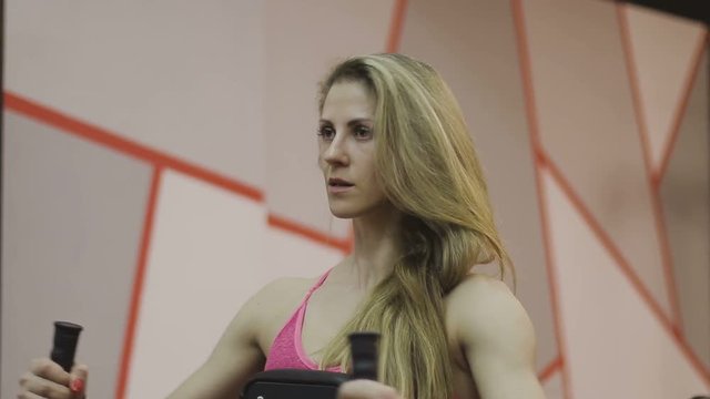 Very beautiful female trainer trains on a fitness machine in a fitness club.