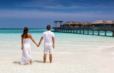 Paar in weißer Kleidung steht am tropischen Strand Hand in Hand