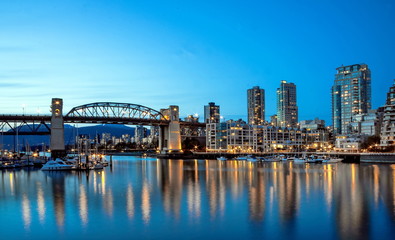 Fototapeta na wymiar Reflections of city lights in the mirror water of the bay at sunset. Burrard Bridge, Downtown of Vancouver City, British Columbia Canada.