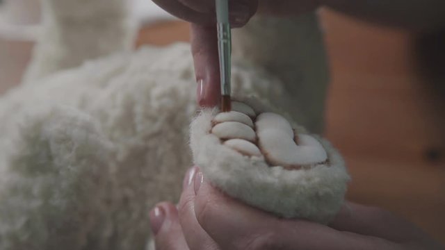 A thin brush in the hands of the artist to create soft toys. The process of creating a teddy bear: master draws a toy paws. Master draws the dividers on foot for a teddy bear in an old-fashioned style