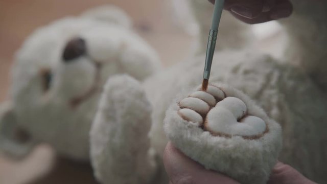 A thin brush in the hands of the artist to create soft toys. The toy is made in classic style. The process of creating a teddy bear: the master draws a toy paws. Handmade toys.