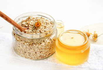 Home spa skincare ingredients. Glass jars of oatmeal flaks and yellow honey, white bathroom towel. 
