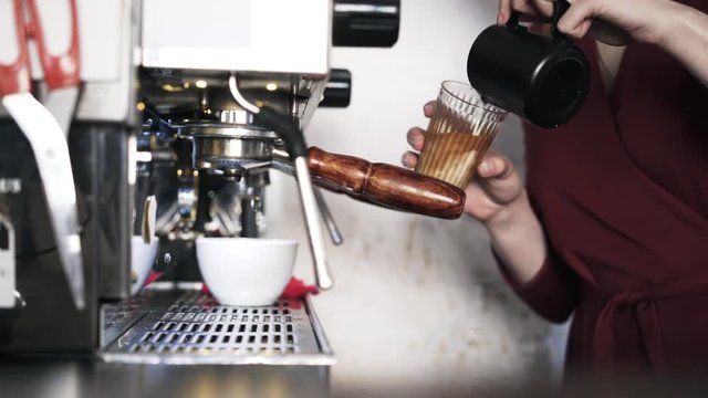 Close up of woman barista s hands adding milk to coffee in a glass. Locked down real time close up shot