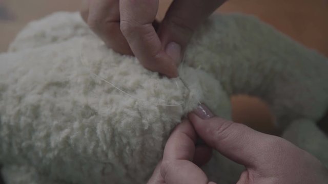 Female hands sew a teddy bear in an old-fashioned style. Concept: a favorite toy of children is a teddy bear. Needle and thread in the hand of a woman - she sews the details of a soft toy.