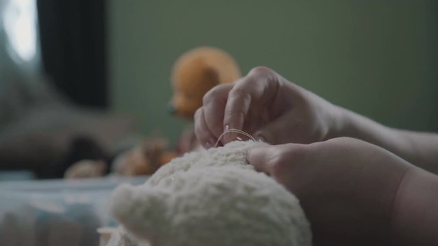 Creating soft handmade toys. Broken toy vintage bear cub - restoration of an old toy. Needle and thread in the hand of a woman - she sews the details of a soft toy. Sewing the details of a toy.