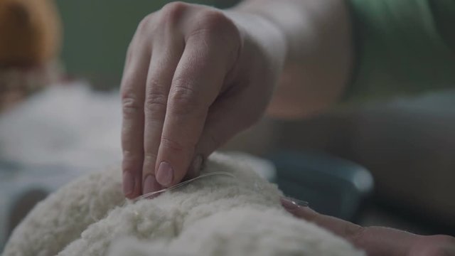 Repair of plush toys: female hands sew a teddy bear. Creating soft handmade toys. Broken toy vintage bear cub - restoration of an old toy. Sew a soft toy: the seam on the back. Handmade process.