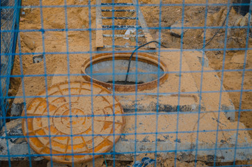 Fototapeta na wymiar An outdoor drainage hatch on the construction site is fenced with a blue mesh. Near the metal ladder and black wire.