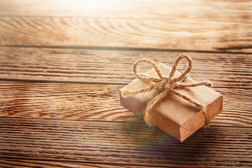 Gift box in kraft paper with bow on wooden background