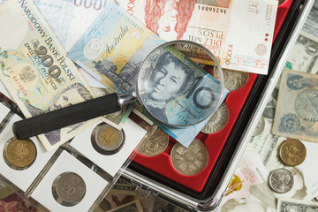 Different collector's coins and banknotes with a magnifying glass