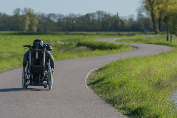 Fototapeta na wymiar A disabled person in a wheelchair going along a long and winding road