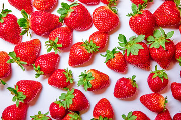 Berries of strawberries of different shapes and sizes are scattered randomly on a white background.