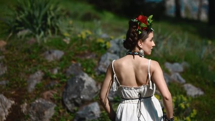 Young female model in traditional mexican dress in image of Frida Kahlo with red wreath on her head posing outdoor under heavy sunshine. Backstage.