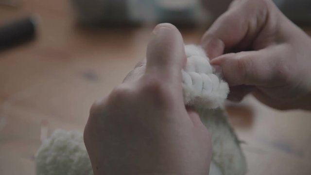 The concept of exclusive work. Craft production. Details and elements of a soft plush toy: female hands sew parts of a toy. Handmade. A rare collectible toy is a teddy bear.