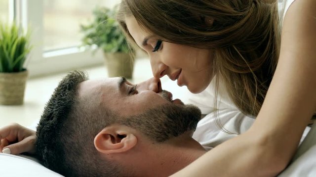 Closeup of Young beautiful and loving couple play and kiss in bed at the morning. Attractive man kissing and hugging his wife in bed